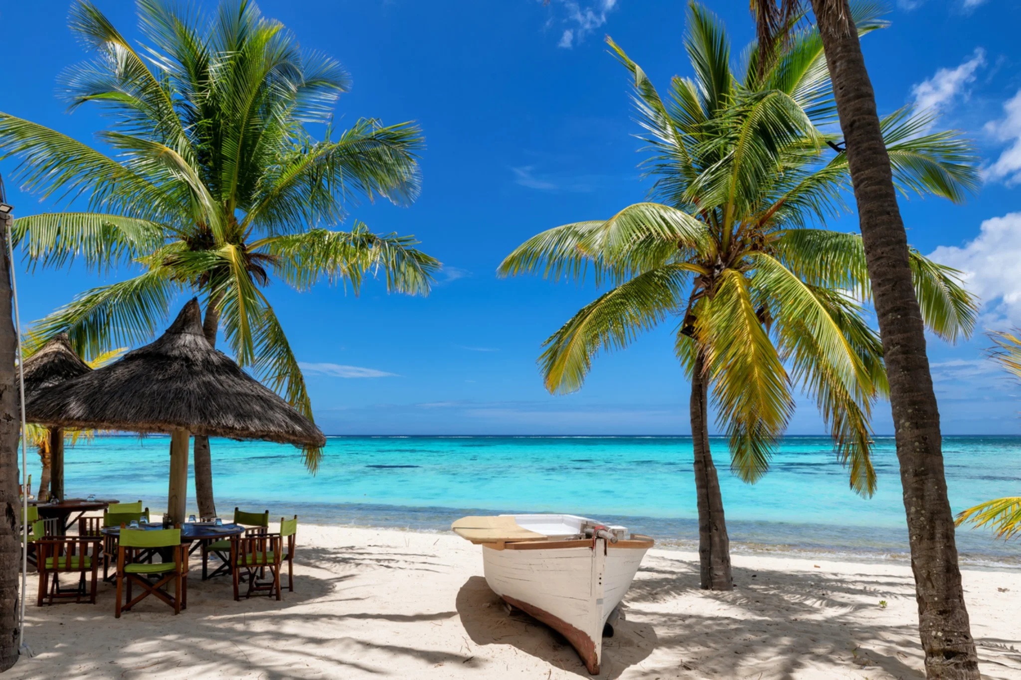 Plage de sable blanc bordée de palmiers avec bateau traditionnel à l’île Maurice