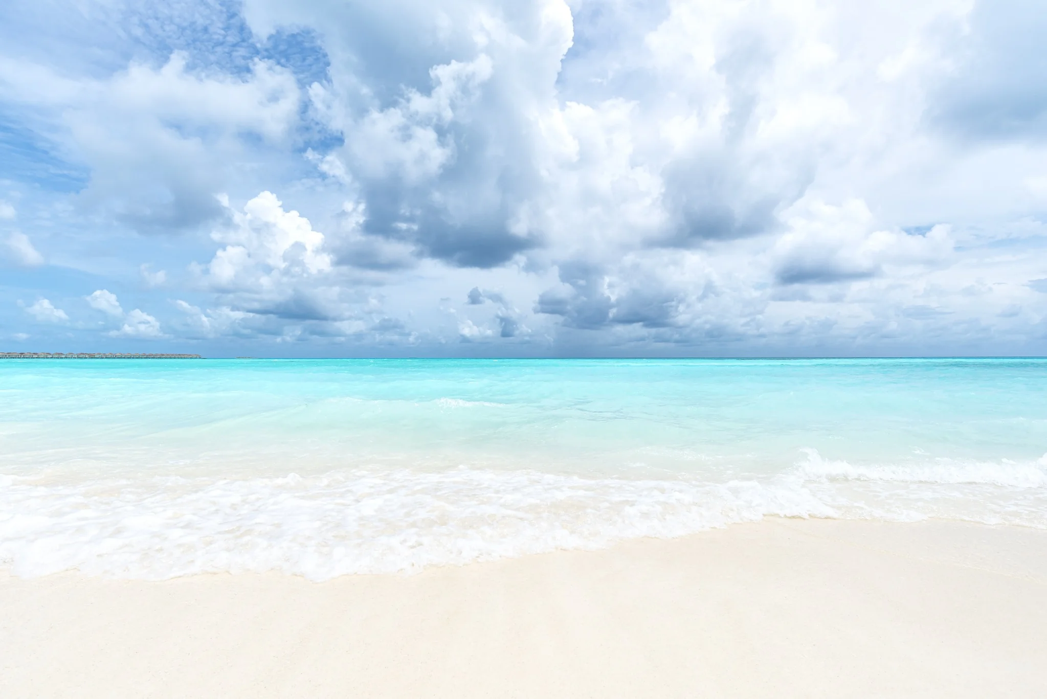 Plage de sable blanc et lagon turquoise sous un ciel légèrement nuageux aux Maldives