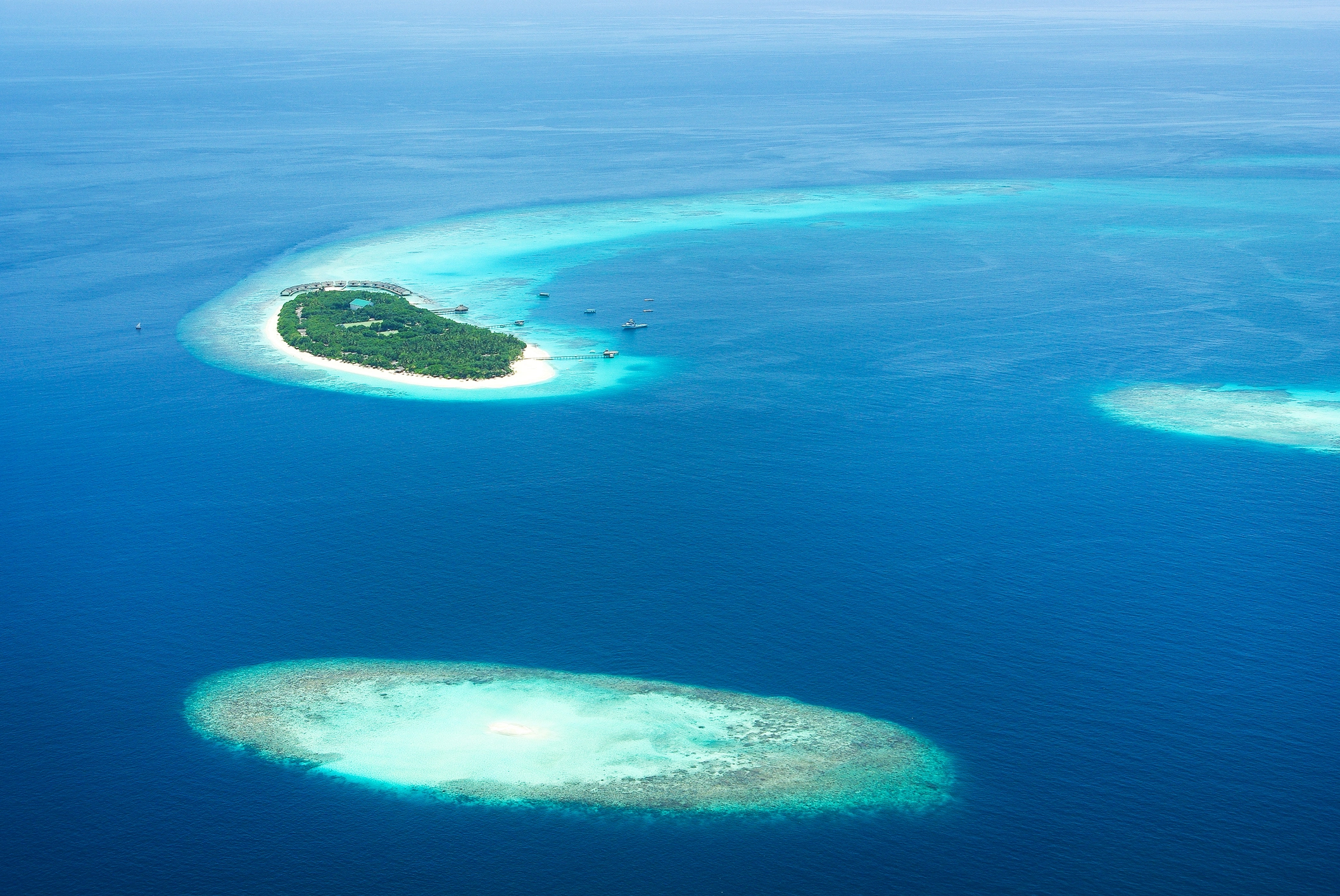 Vue aérienne d’une île-hôtel entourée d’un lagon turquoise et de récifs aux Maldives