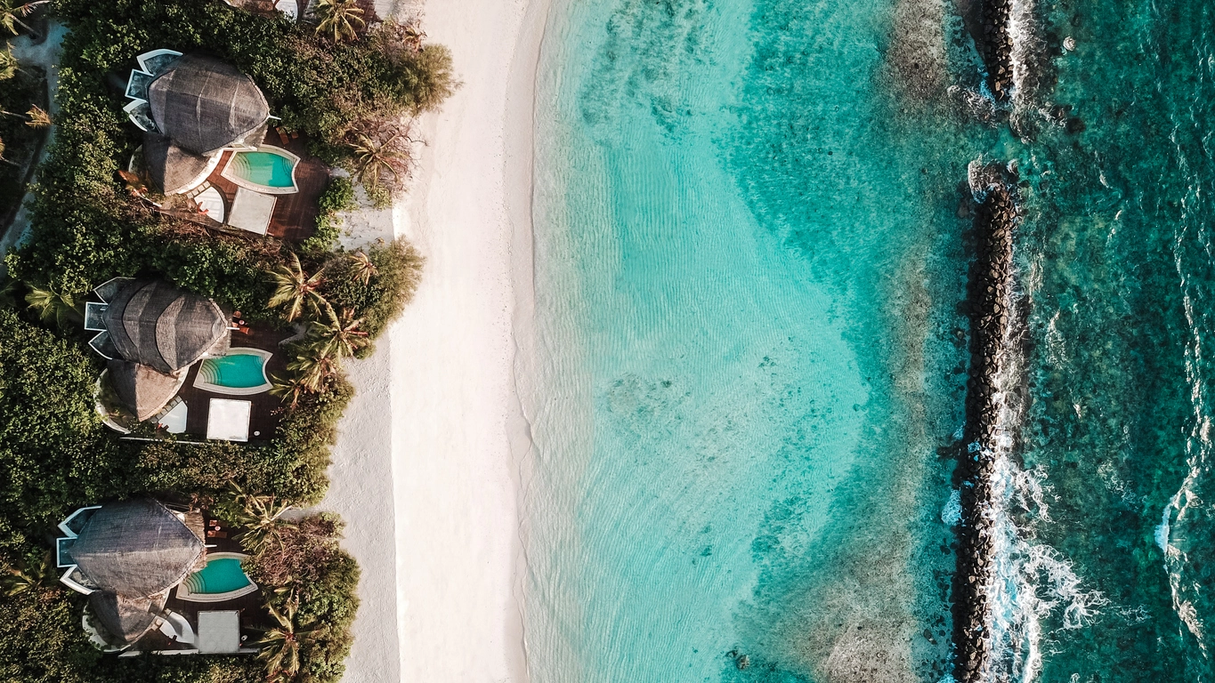 Vue aérienne de villas de luxe en bord de plage face à un lagon turquoise aux Maldives